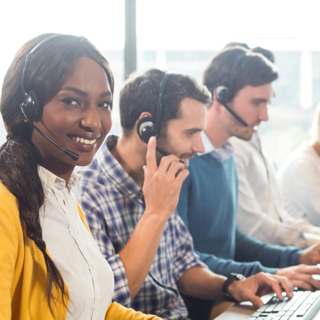 Team working on computer with headset while a colleague smiling at camera in the office
